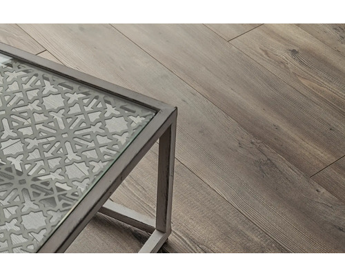 Imagine detaliată a unei mese cu blat de sticlă și model decorativ, lângă o podea de lemn.