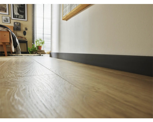Prim-plan al unei podele laminate cu o plintă întunecată într-un dormitor.