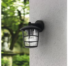 Lumină de perete exterioară neagră cu abajur transparent pe un perete de casă