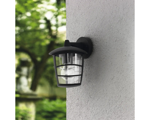 Lumină de perete exterioară neagră cu abajur transparent pe un perete de casă