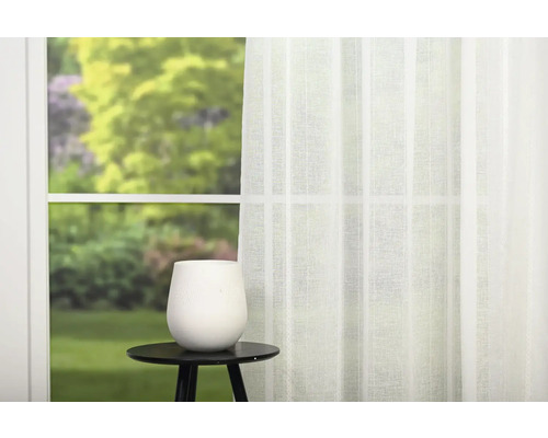 Cameră luminoasă cu perdea, vază și măsuță laterală în fața ferestrei cu vedere la grădină