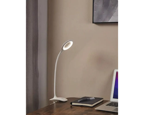Scenă de birou cu o lampă de birou cu clemă LED albă lângă un caiet și un laptop