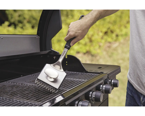 O persoană curăță grătarul cu o perie de grătar.