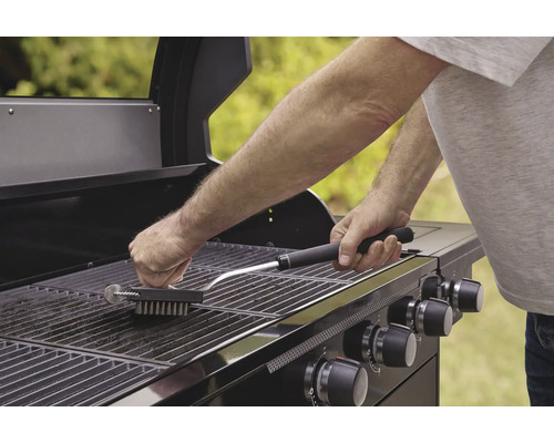 O persoană curăță un grătar cu o perie pentru grătar.