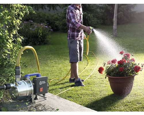 Un bărbat udă flori cu o pompă de grădină și un furtun de grădină într-o grădină.