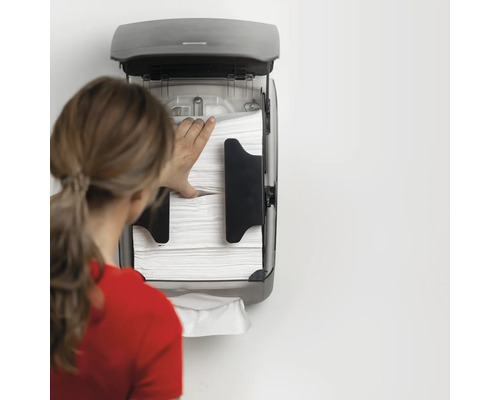 Femeia umple un suport pentru prosoape de hârtie de perete cu prosoape de hârtie