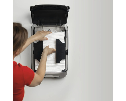 O persoană reumple un dozator de prosoape de hârtie de pe un perete cu prosoape de hârtie.