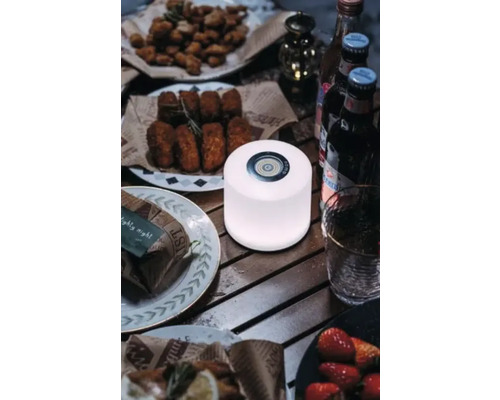 Scenă cu o masă rotundă cu mâncare și băuturi, cu o lumină rotundă în centru.