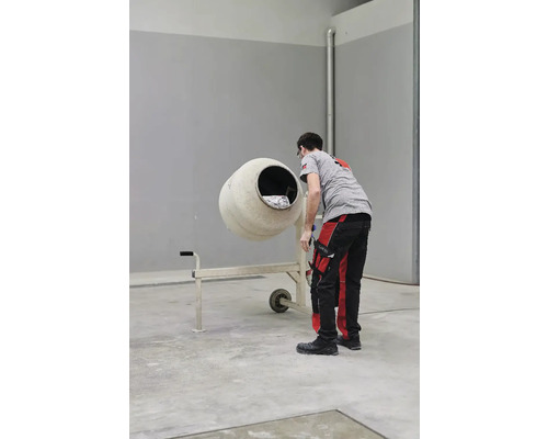 Un muncitor în construcții stă lângă un mixer de beton.