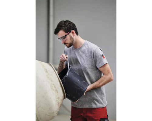 Un bărbat cu ochelari de protecție goleşte o găleată într-un mixer de ciment.