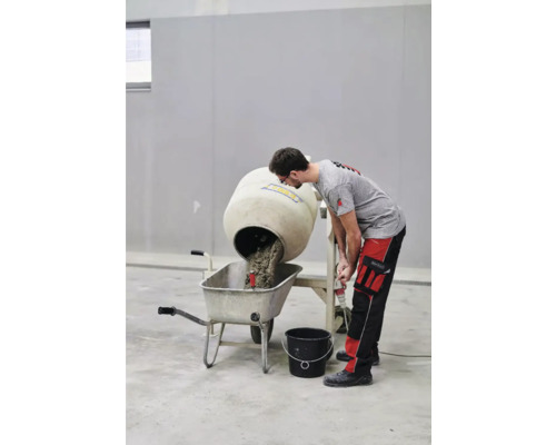 Un bărbat descarcă un mixer de beton într-o roabă