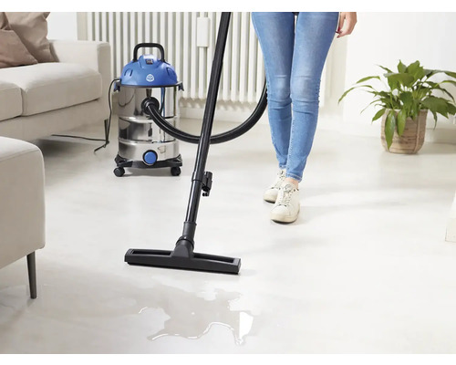 O persoană folosește un aspirator umed uscat pentru a curăța o cameră luminoasă în care se află o canapea și o plantă de interior