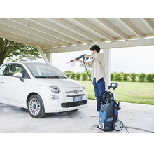 O persoană curăță o mașină albă cu un aparat de spălat cu presiune sub un carport.