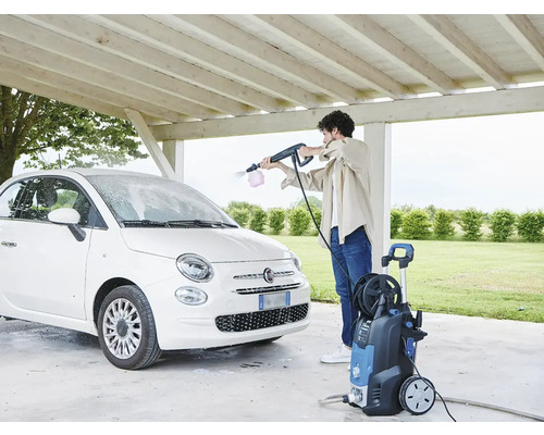 O persoană curăță o mașină albă cu un aparat de spălat cu presiune sub un carport.