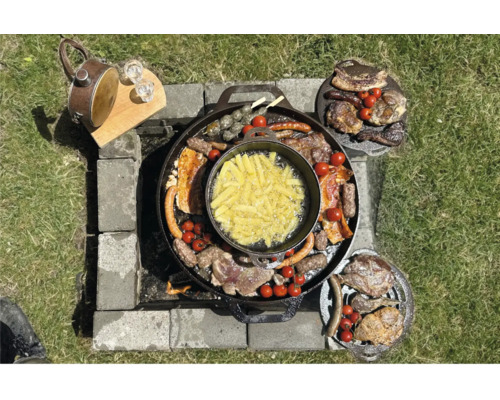 Scenă de grătar cu carne, cârnați, legume și cartofi prăjiți pe o plită, completată de un ceainic și băuturi pe o masă din lemn.