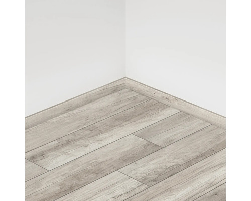 Pardoseală laminată cu aspect de lemn și plinte albe într-un colț