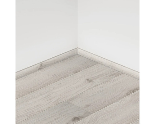 Suprafață de podea laminată deschisă la culoare cu plintă pe un perete alb