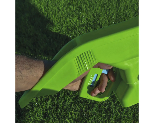 Prim-plan cu o mână care operează un distribuitor verde pe un gazon.