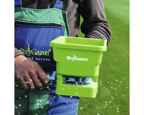 O persoană folosește un distribuitor de îngrășăminte pentru îngrijirea gazonului.